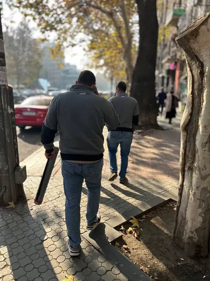 Two engineers walking away down a tree-lined Yerevan street carrying their kit, on the way between sites
