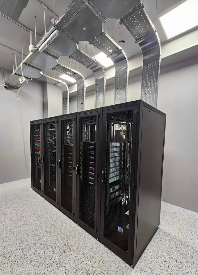 A completed row of five black server cabinets in a data centre room, each fed from above by its own galvanised tray drop