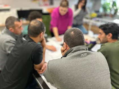A working session with the drawings laid out, one colleague standing over the table and the rest of the team following along