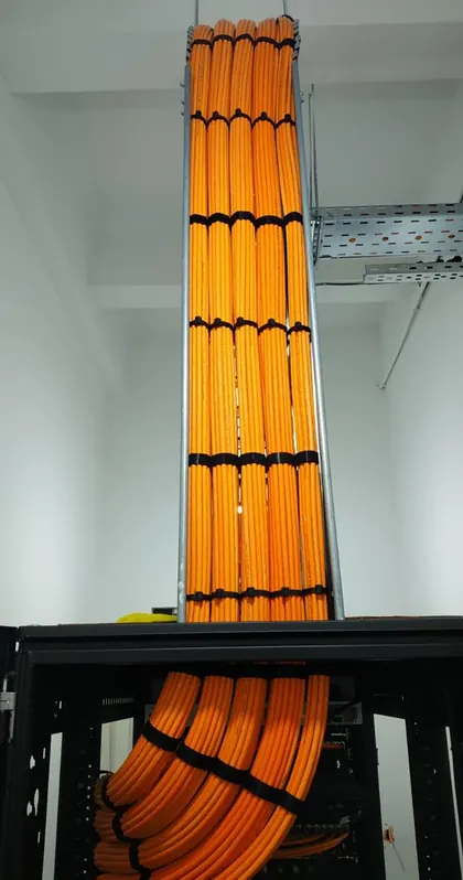 Orange fibre optic cabling running vertically in a riser from ceiling to cabinet, banded at regular intervals and fanned into the rack below