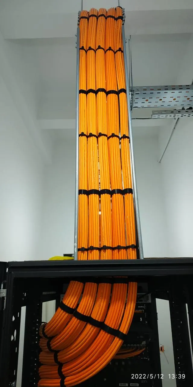 Orange fibre optic cabling running vertically in a riser from ceiling to cabinet, banded at regular intervals and fanned into the rack below