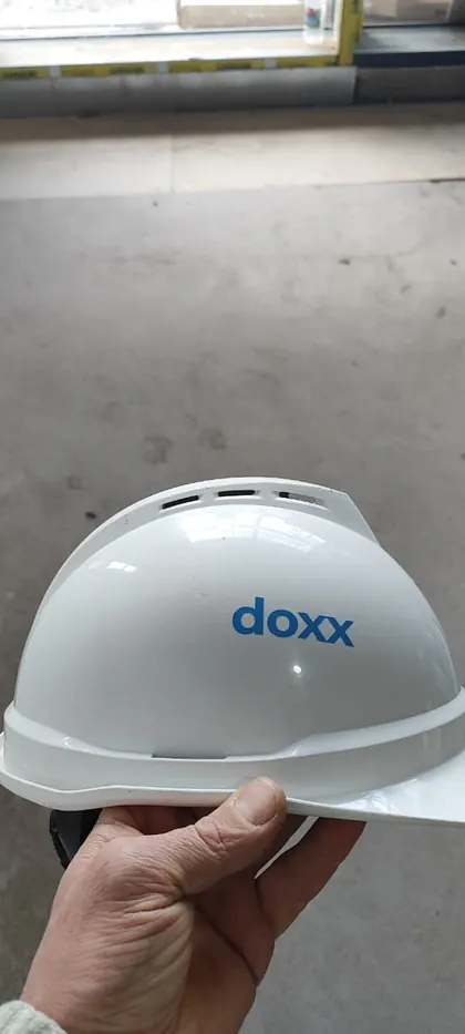 A hand holding out a white hard hat carrying the logo of DOXX, the system integrator STP delivers alongside