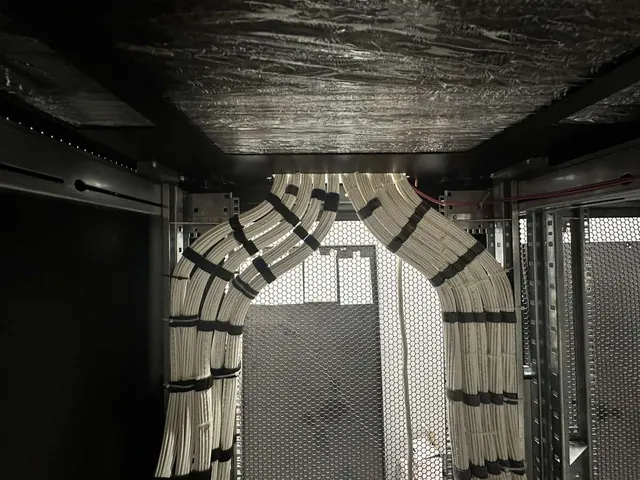 Structured cabling entering a rack in two symmetrical sweeping bundles, each run combed flat and secured at regular intervals with hook-and-loop ties