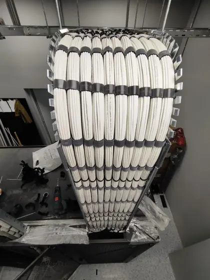 A large bundle of white twisted pair cables fanning from an overhead tray down into a cabinet, each cable laid parallel without crossovers