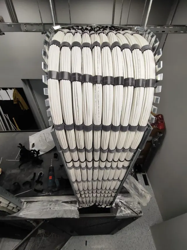 A large bundle of white twisted pair cables fanning from an overhead tray down into a cabinet, each cable laid parallel without crossovers